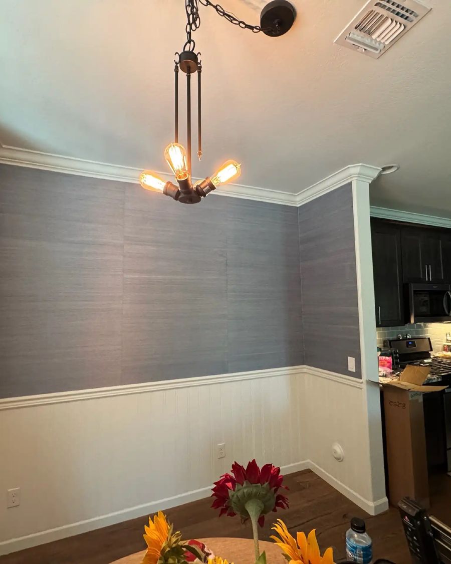 Dining room with blue-grey grasscloth above white wainscoting and an iron pendant light