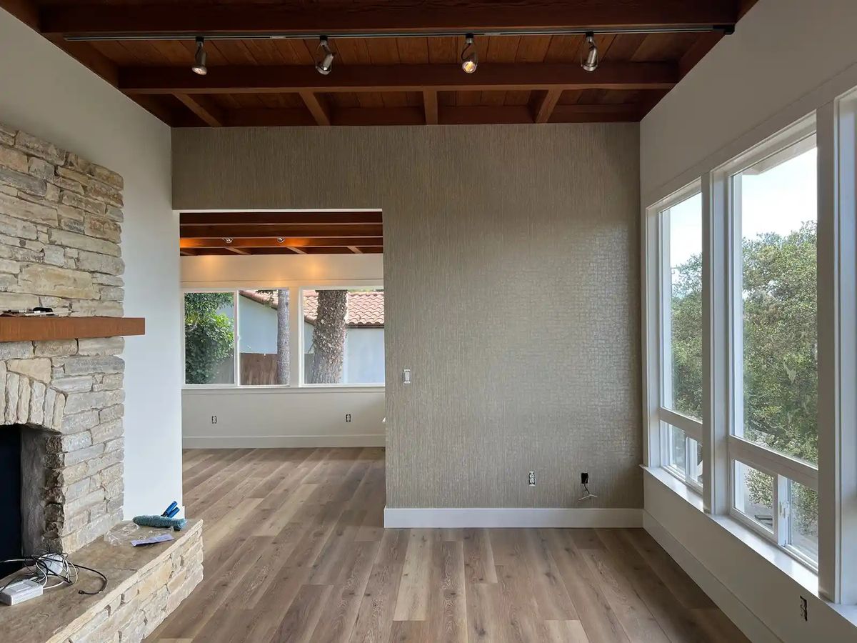Living room with a stacked-stone fireplace, a warm-toned textured wallcovering and a wood-plank ceiling