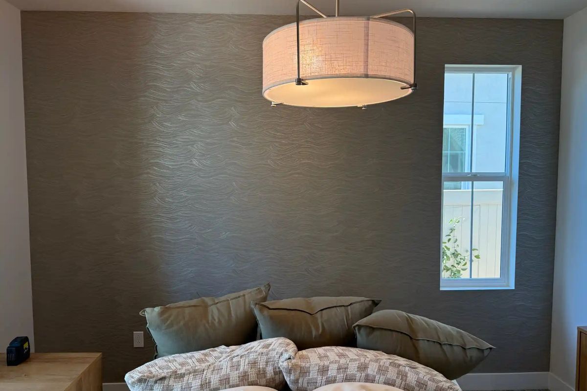 Bedroom accent wall in a soft brown textured wallcovering under a linen drum pendant