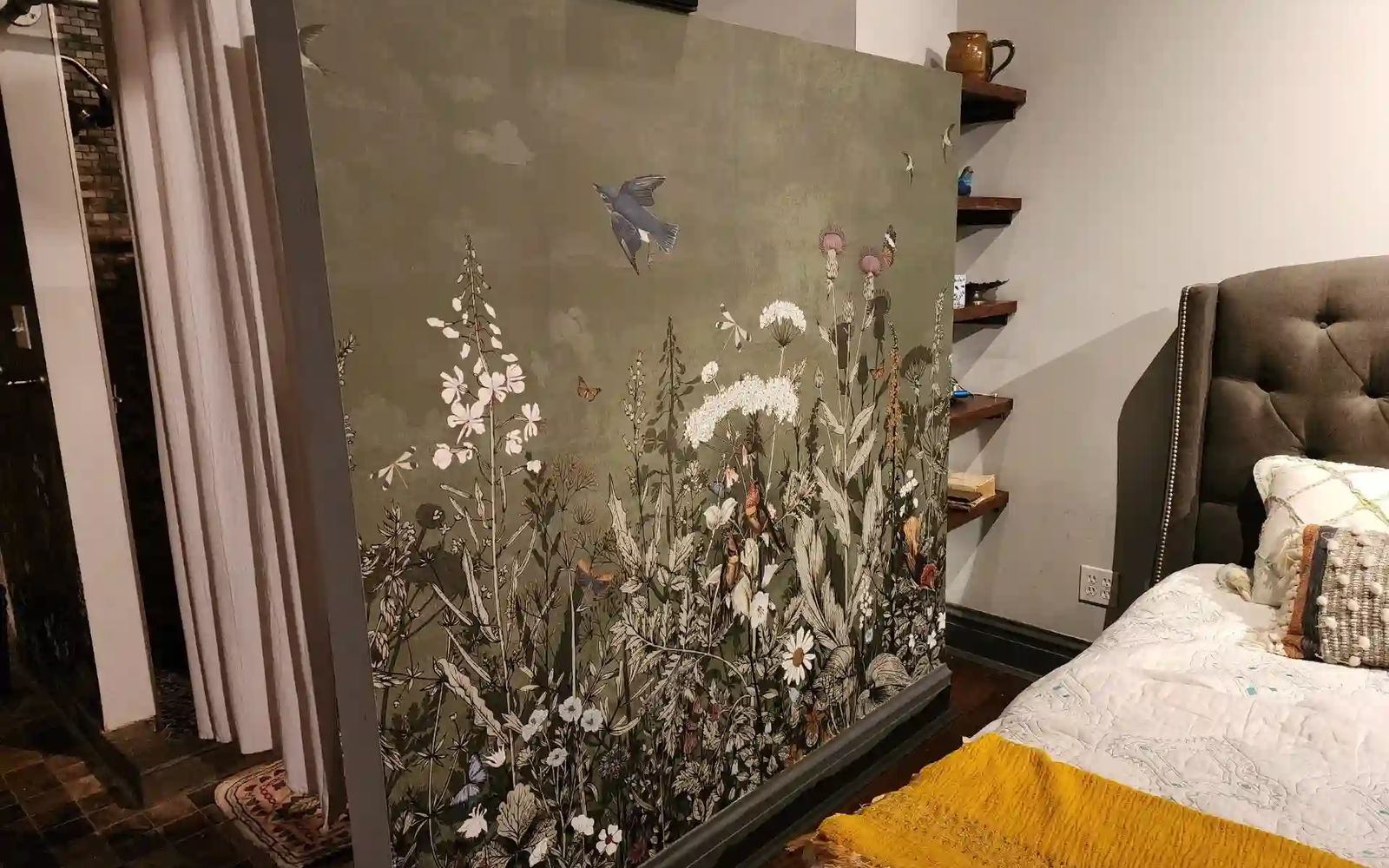 Bedroom wall covered in a sage-green wildflower mural with white blooms, next to a tufted headboard