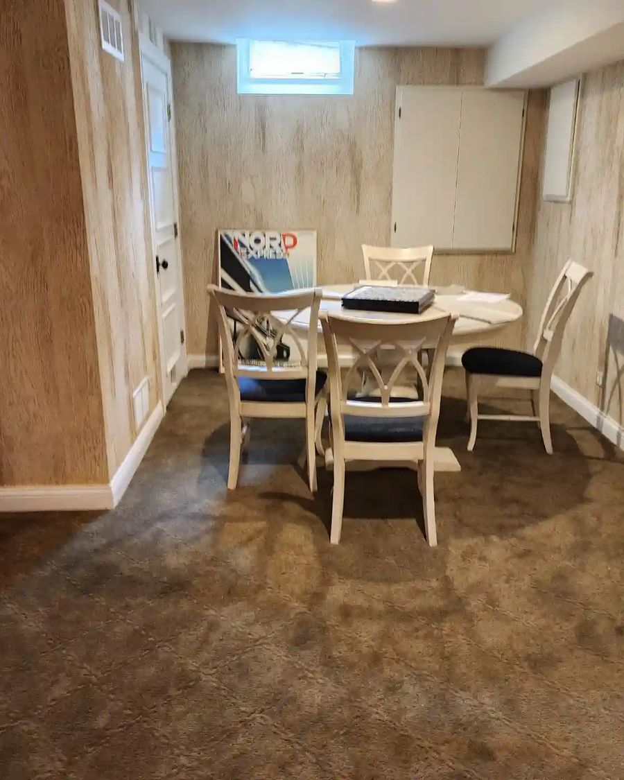 Dining area with weathered wood-plank print wallpaper on every wall and white cross-back chairs