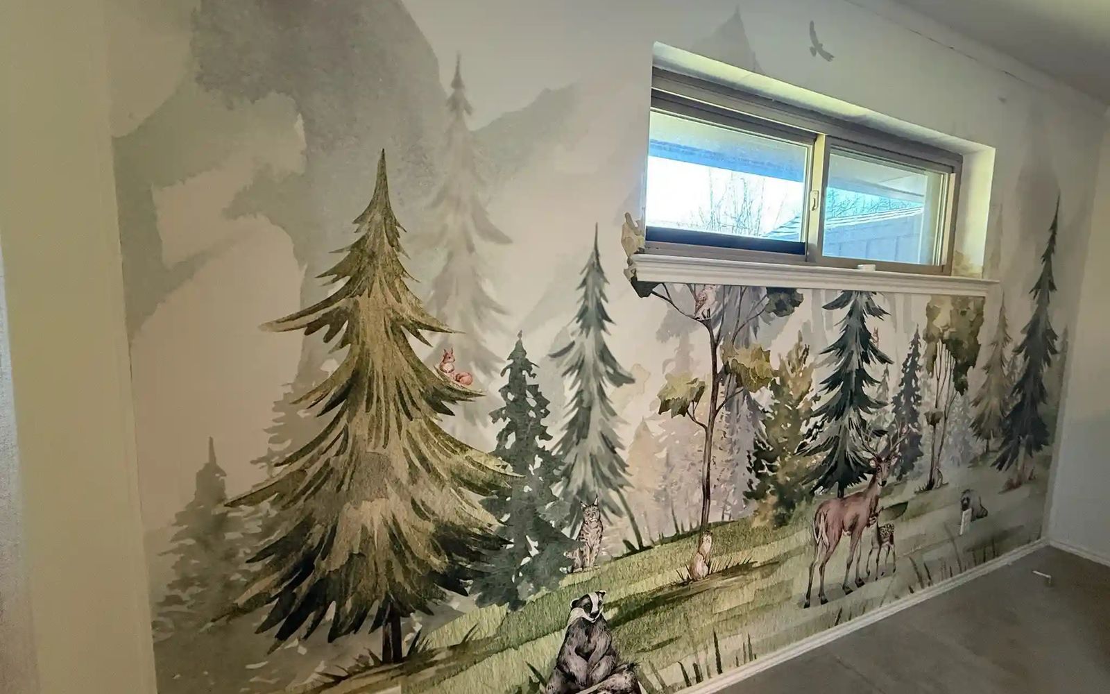 Room wall with a watercolor woodland mural of pine trees, deer and small animals around a window